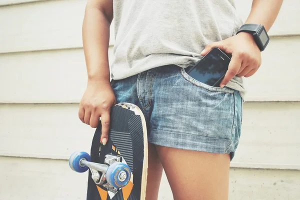 Telefone inteligente no bolso de jeans com skate — Fotografia de Stock