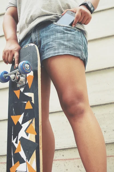 Telefone inteligente no bolso de jeans com skate — Fotografia de Stock