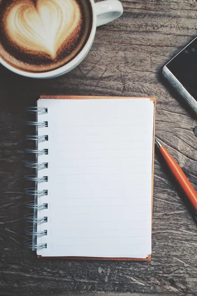 Bloco de notas em branco e telefone inteligente com café arte latte na mesa de escritório — Fotografia de Stock