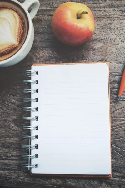 Bloco de notas em branco e maçã com café de arte latte na mesa de escritório — Fotografia de Stock