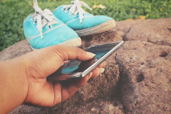 Жінка використовує смартфон з кросівками — стокове фото