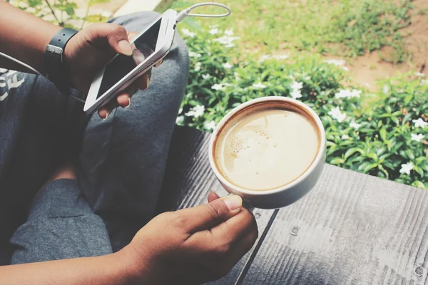 Mujer jugando smartphone con auriculares y café en el jardín — Foto de Stock