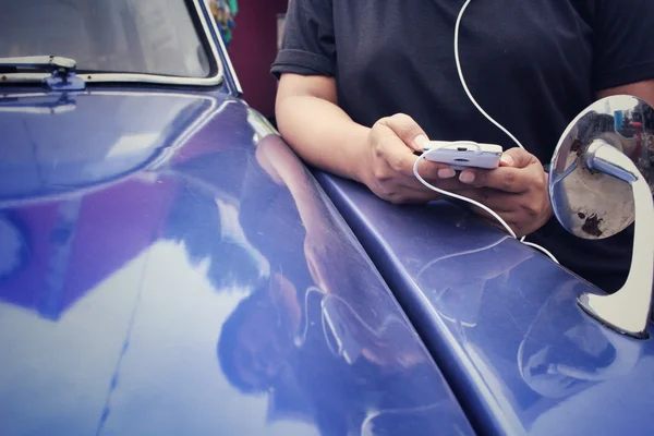 오래 된 자동차와 스마트폰 이어폰에서 음악을 듣고 하는 여자 — 스톡 사진