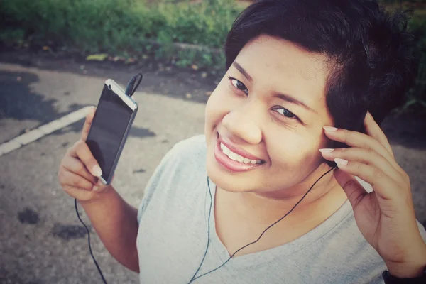 Mujer escuchando música en auriculares con teléfono inteligente — Foto de Stock
