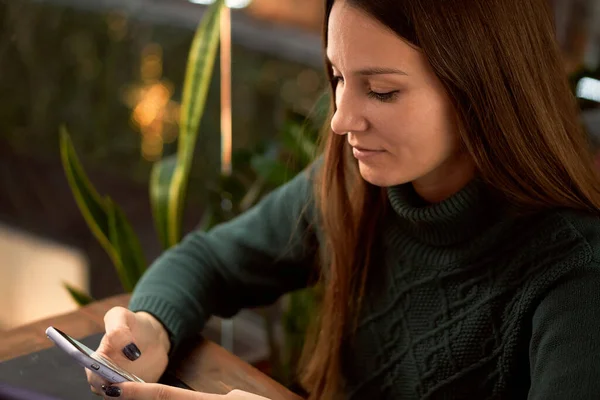 Young brunette woman in cafe with laptop communicates by smartphone