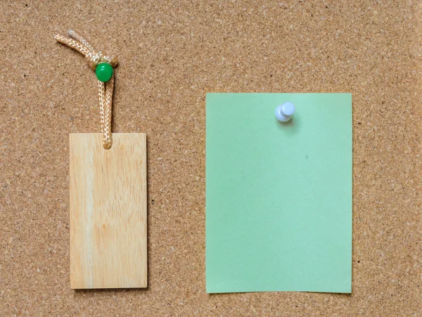 Blank wooden tag and paper on cork board — Stock Photo, Image