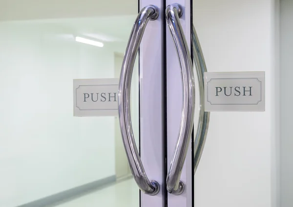 Chrome handles with push sign on glass door — Stock Photo, Image