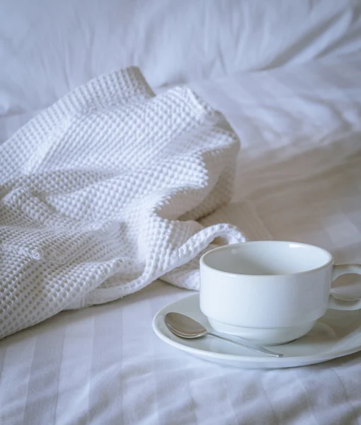Kaffeetasse mit weißem Bademantel auf dem Bett — Stockfoto