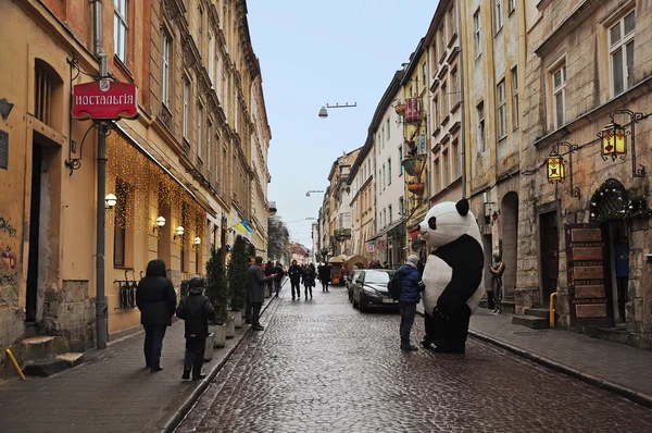 Lviv, Ucrania - 24 de enero de 2015: Paisaje urbano de Lviv. Vista de la calle Lviv con la arquitectura antigua y la gente caminando. Gran panda entretiene a los turistas . — Foto de Stock