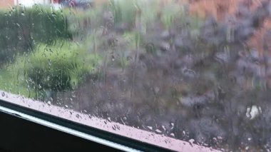 Yağmurdan sırılsıklam olmuş bir pencerenin yakın çekimi, camlardan süzülen damlacıklar, dışarıda yumuşak, bulanık bir bahçe. Huysuzluk, kapalı mekanlarda rahat günler ve yağmurlu havayı çağrıştırıyor..