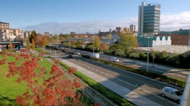 Valladolid, İspanya - 21 Kasım 2025: İspanya 'nın Valladolid kentindeki sonbahar kırmızı ağaçları ve Bilim Müzesi ile canlı bir şehir caddesi. Yeşil çitlerin yanında geniş bir yol boyunca arabalar gider..