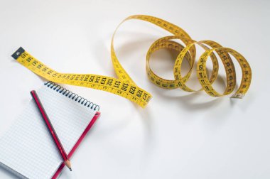 Temiz beyaz bir yüzey üzerinde küçük bir kılavuz ve kalem yanında sarı bir mezura açılır, planlama, ölçüm, DIY, tasarım ve zanaat projelerini çağrıştırır..