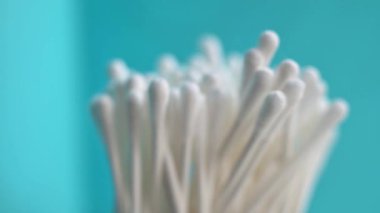 Beyaz pamuklu çubukların yumuşak odaklı yakın plan görüntüsü turkuaz bir zemine karşı dik olarak dizilmiş. Kişisel bakım, güzellik, cilt bakımı veya hijyen ürünleri listesi ve editörlük özellikleri için ideal.