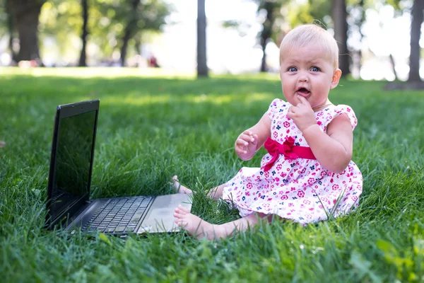 Dziewczynka siedzi na zielonej trawie z laptopa — Zdjęcie stockowe