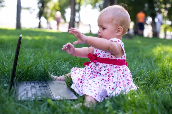 Dizüstü bilgisayar ile yeşil çimenlerin üzerinde oturan kız bebek — Stok fotoğraf