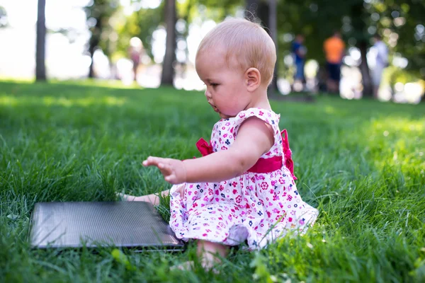 Baby girl sitting on the green grass with laptop — Stock Photo, Image