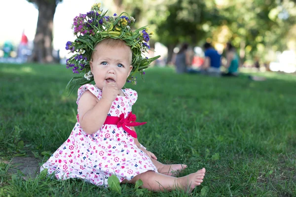 Petite fille avec une couronne sur une tête et un bouquet dans les mains sur une clairière de pissenlits — Photo