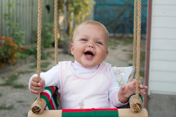 Kıvırcık saçlı bir güneşli yaz Bahçesi bir parkta salıncak binmek zevk mavi bir elbise giymiş mutlu gülen yürümeye başlayan çocuk kız — Stok fotoğraf