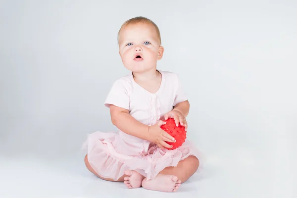 Feliz niña en un vestido corto de color rosa lanza una gran bola a rayas — Foto de Stock