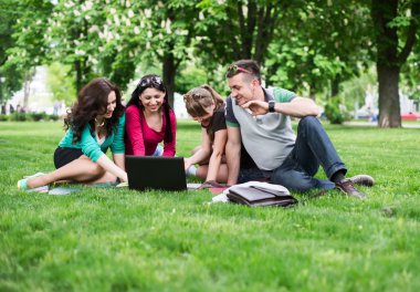 Grup çimlerde oturan genç üniversite öğrencilerinin