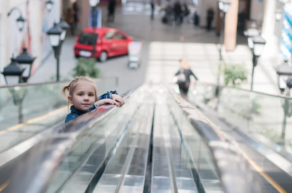 Lindo niño pequeño en el centro comercial de pie en la escalera móvil, escaleras mecánicas —  Fotos de Stock