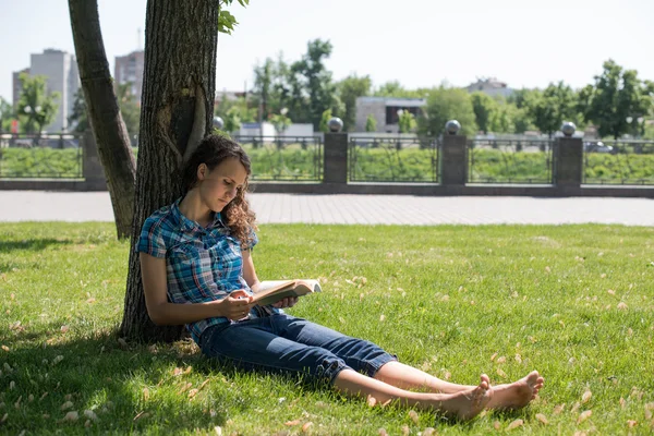 Giovane bella donna attenta si trova su erba verde e legge libro — Foto Stock