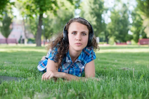 Ein lächelndes junges Mädchen mit Laptop im Freien, das per Kopfhörer Musik hört — Stockfoto