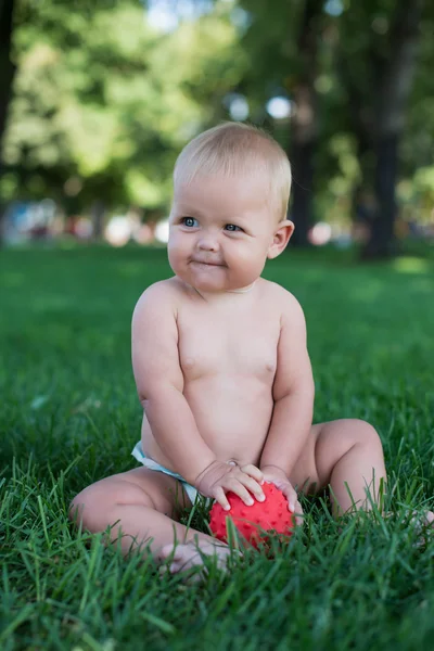 Мальчик сидит на траве в парке, играет с мячами и улыбается . — стоковое фото