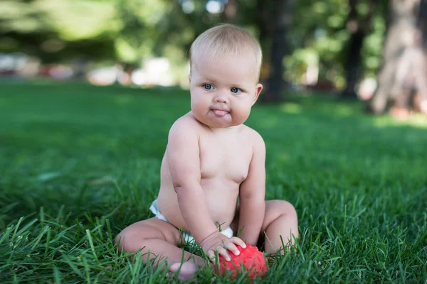 Boy sitting on grass in park, playing with balls and smiling. — Stock Photo, Image