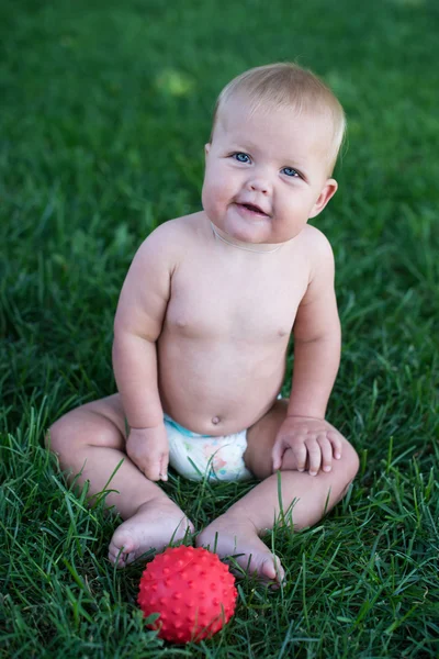 Menino sentado na grama no parque, brincando com bolas e sorrindo . — Fotografia de Stock