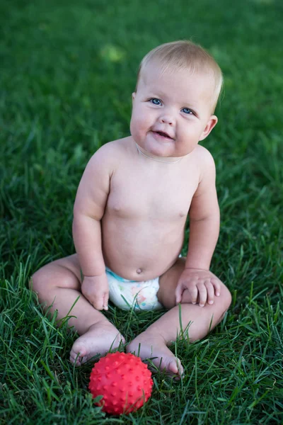 Boy sitting on grass in park, playing with balls and smiling. — Stock Photo, Image