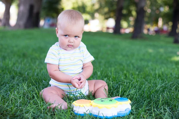 Bébé heureux avec des cheveux légers et pelucheux assis sur l'herbe et riant . — Photo