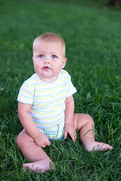 Ребенок в зеленом жилете сидит на траве и плачет — стоковое фото