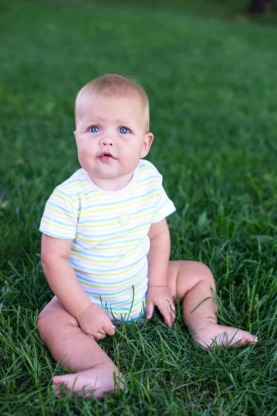 Un bébé dans un gilet vert assis sur l'herbe et pleurant — Photo