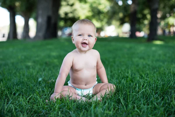 Happy baby with light and fluffy hair sitting on the grass and laughing. Summer and very warm. Happy smile. — Stock Photo, Image