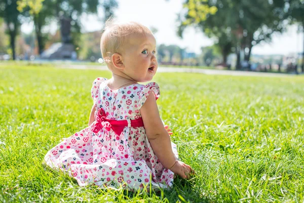 遊び心のある女の子が、草原に座っています。かわいい赤ちゃん. — ストック写真