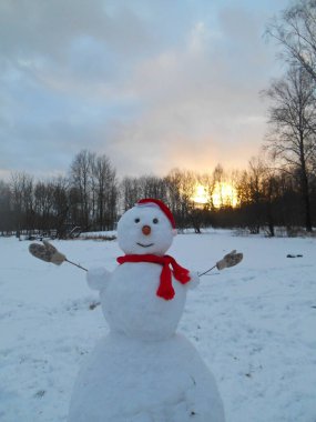 Noel ve Yeni Yıl Kardan Adam kırmızı şapkalı kış manzaralı günbatımı parkında