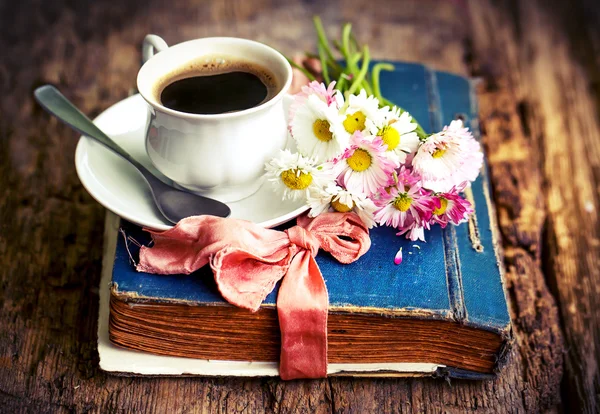 Bir fincan sıcak kahve, çiçekler ve kitap.