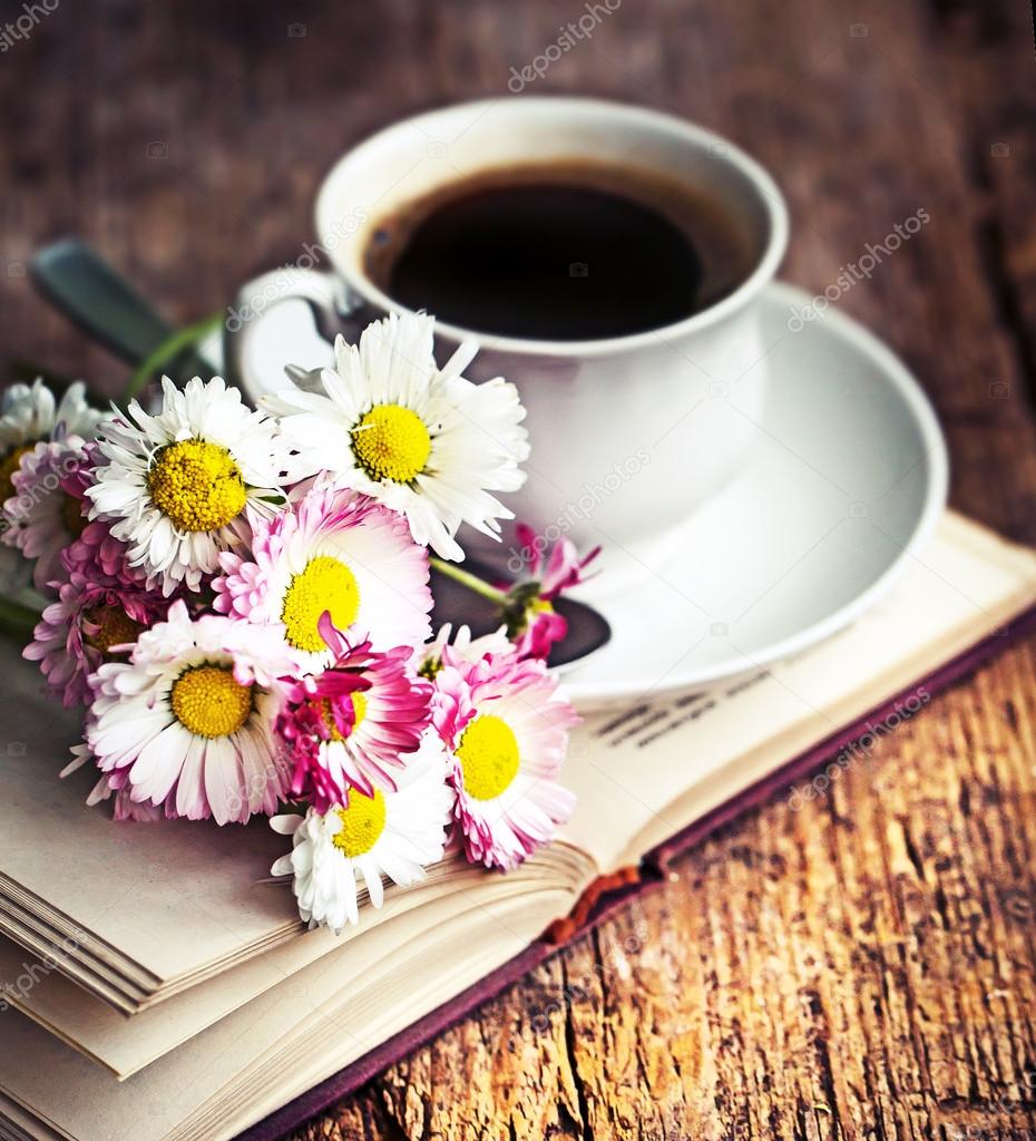 A cup of hot coffee, flowers and book.