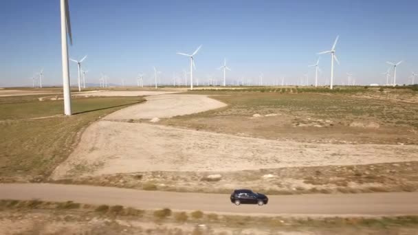 Siguiendo un coche negro en la granja de molinos de viento — Vídeo de stock