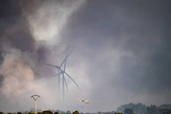 Fumaça, moinhos de vento e helicóptero voando com bambi-balde — Fotografia de Stock