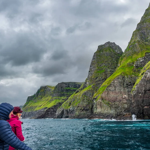 Wazig onherkenbare toeristen over boot observeren indrukwekkende Vestmanna kliffen onder de storm — Stockfoto