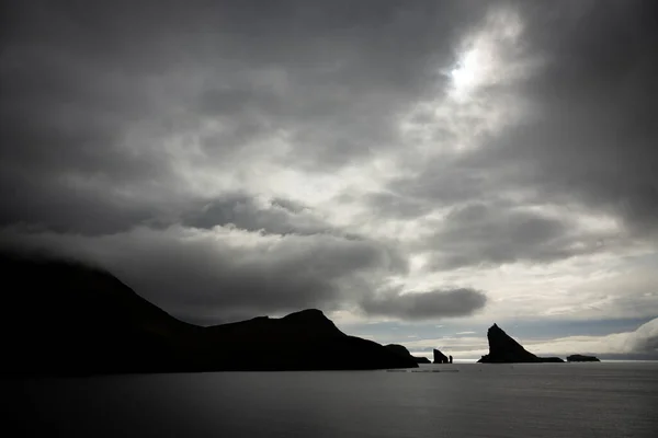 Tindholmur boulder pico contra o céu escuro nublado, retroiluminado — Fotografia de Stock