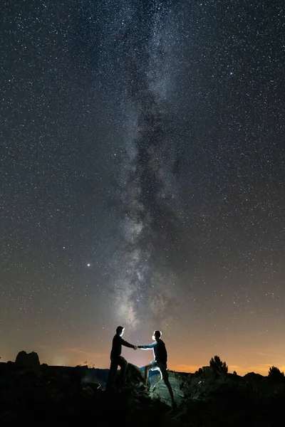 Two persons shaking hands against long milky way — Stock Photo, Image