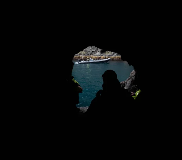 Unrecognizable people looking through cave exit and motorboat — Stock Photo, Image