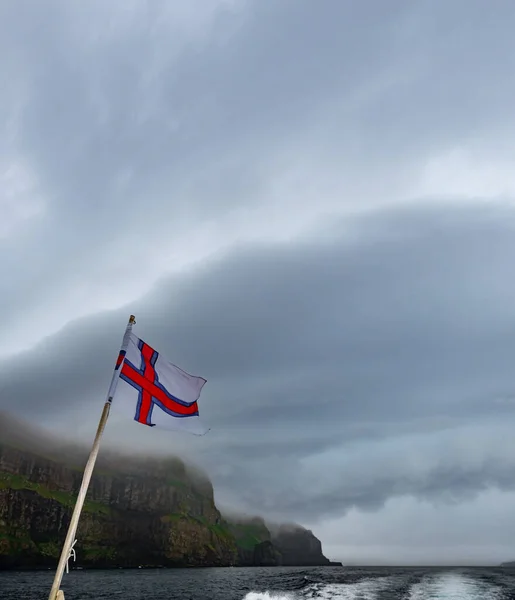 Faeröer vlag onder steile kustlijn en wolken — Stockfoto