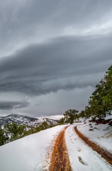 Fırtınalı bulutlar ve yıldırımlarla karın üzerinde tekerlek izleri — Stok fotoğraf