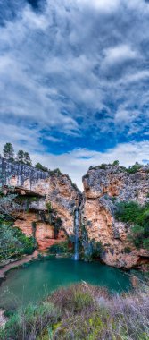 Renkli göleti ve bulutlu gökyüzü olan Idyllic şelalesi