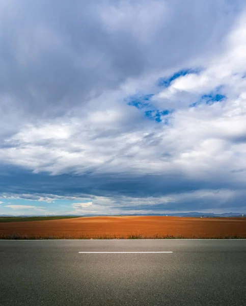 Strada e terreni coltivati sotto cielo nuvoloso — Foto Stock