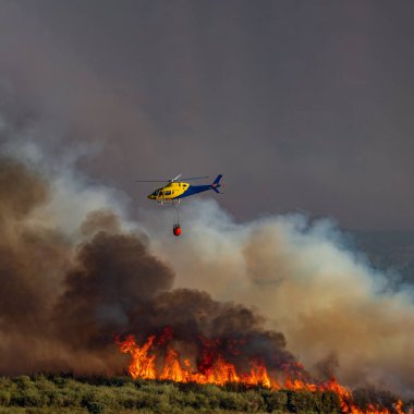 Alevlerin üzerinde bambi kovası olan bir helikopter.